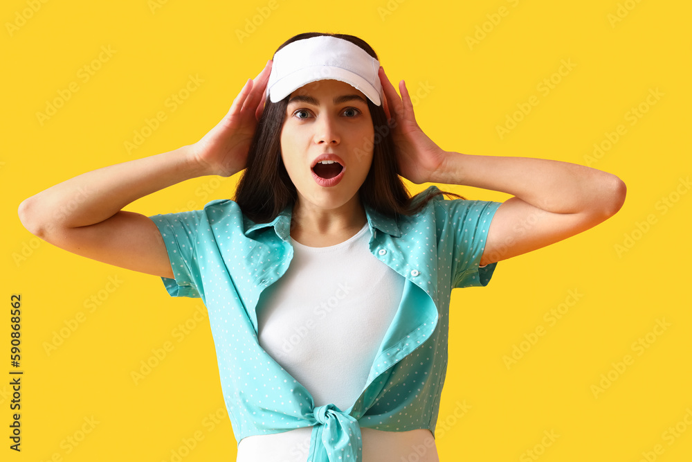 Shocked young woman in cap on yellow background