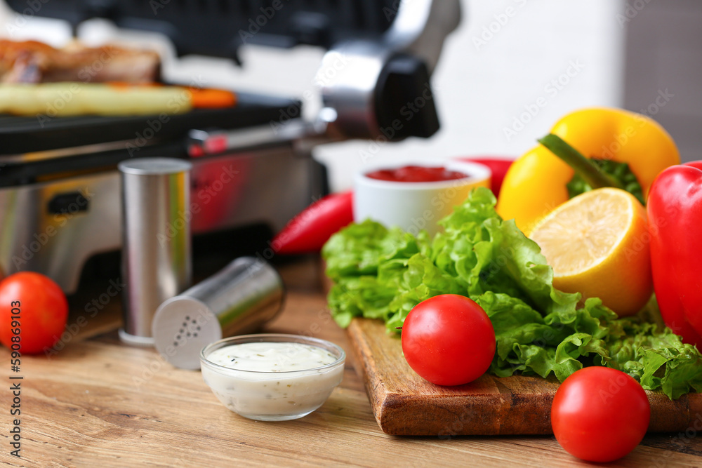 Wooden board with fresh vegetables and bowl of sauce on table in kitchen