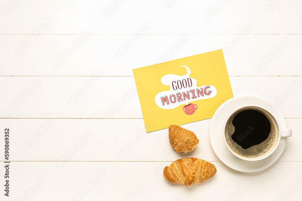 Cup of coffee, tasty croissants and card with text GOOD MORNING on light wooden background