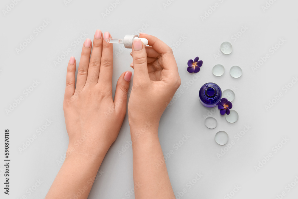 Female hands with bottle of cuticle oil, glass stones and flowers on light background