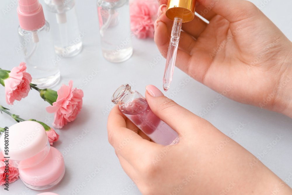 Female hands with bottle of cuticle oil, cosmetics and carnation flowers on light background, closeu