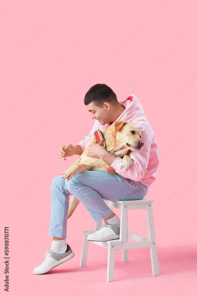 Young man with cute Labrador dog sitting on stepladder against pink background