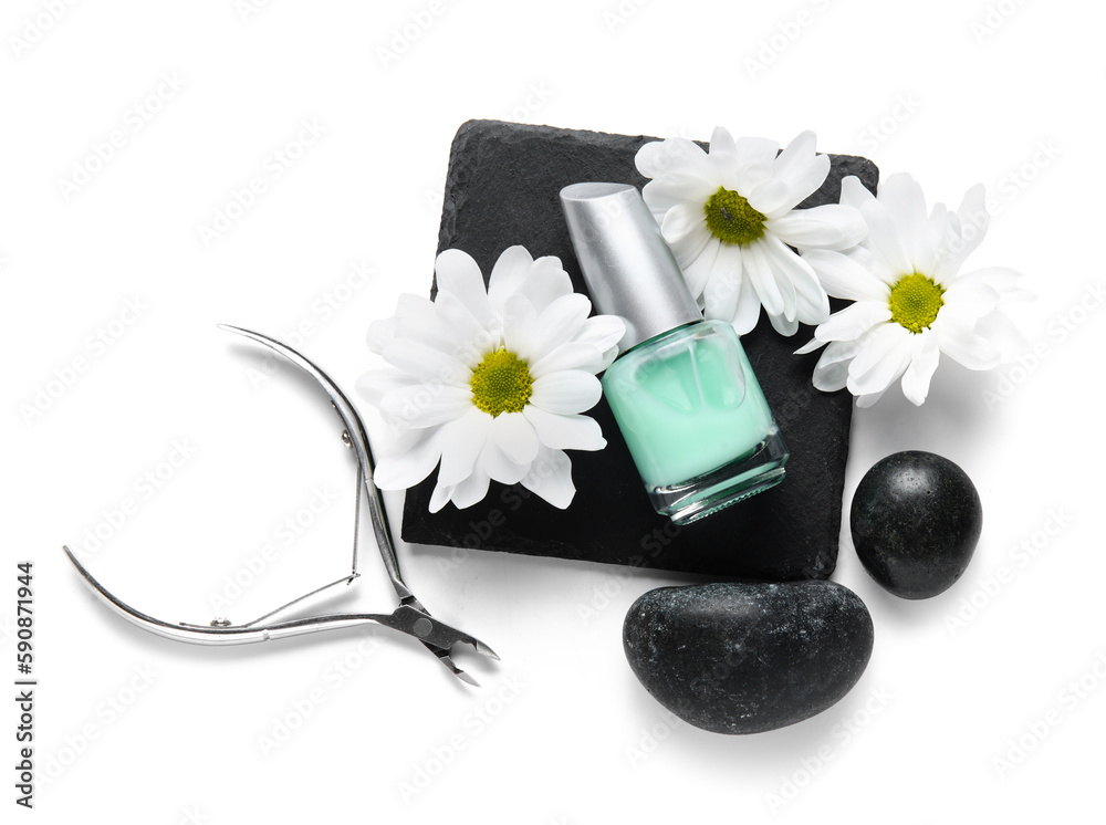 Composition with bottle of cuticle oil, spa stones, nail cutter and chamomile flowers on white backg