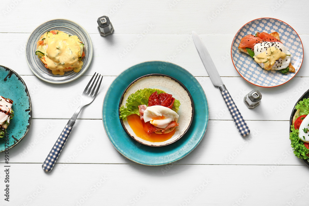 Composition with plates of different eggs Benedict on white wooden table