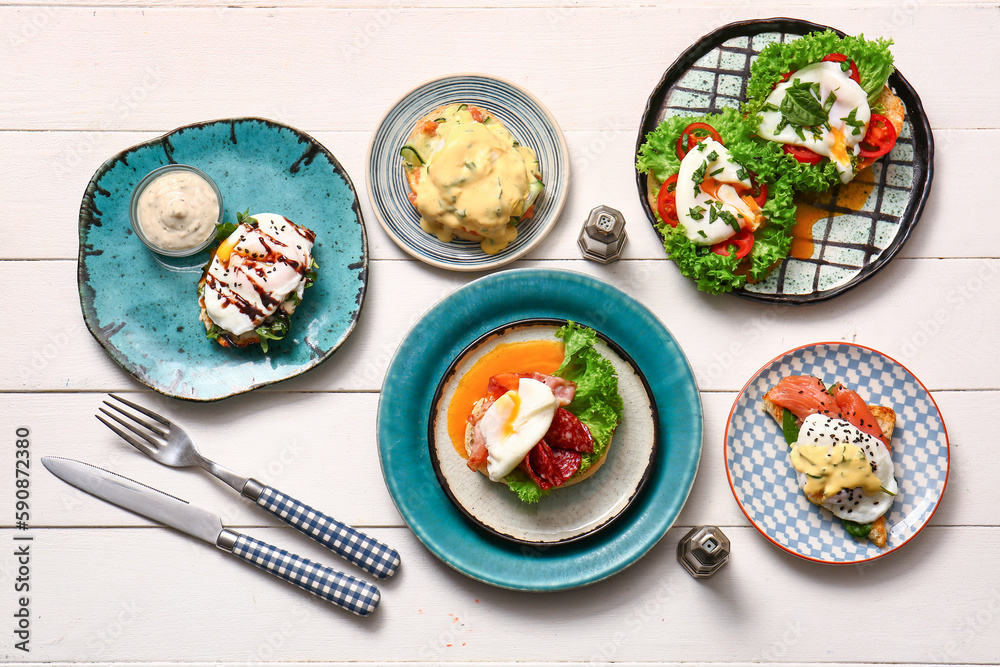 Composition with plates of different eggs Benedict on white wooden table