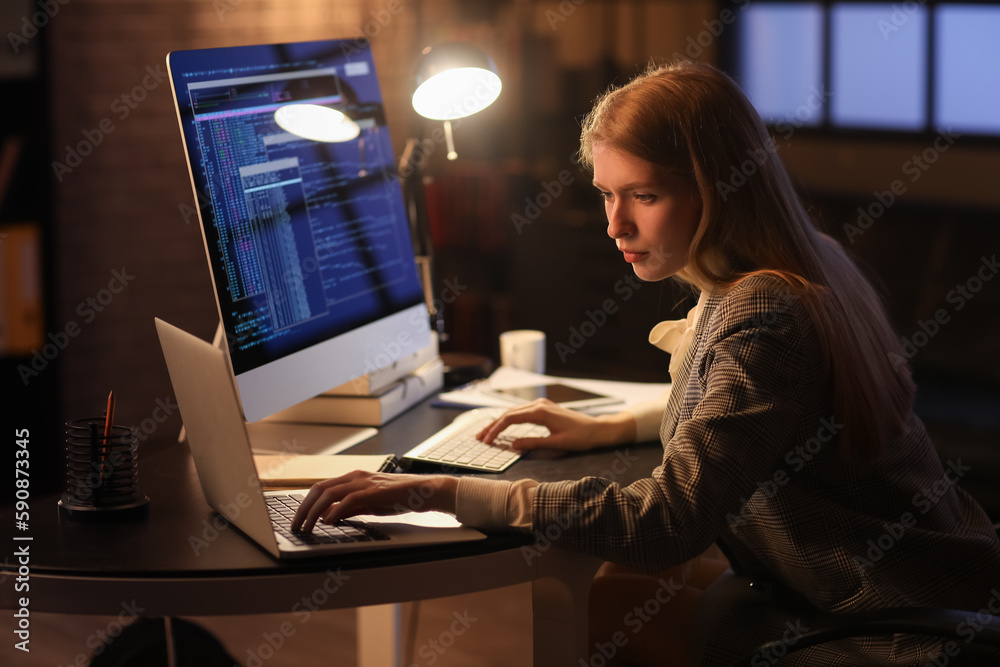 Female programmer working with laptop in office at night