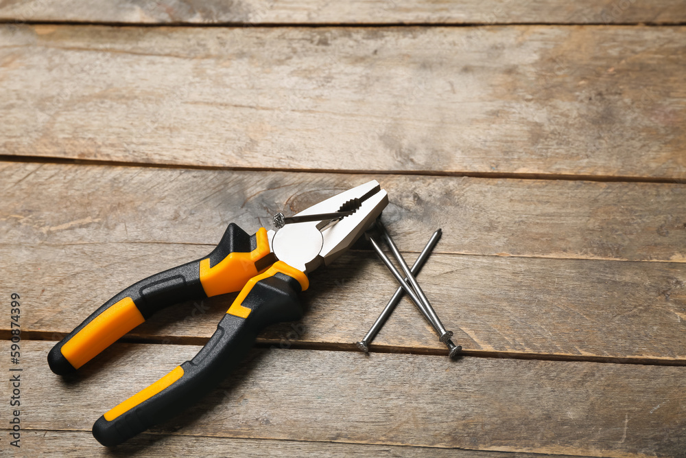 Orange pliers and nails on wooden background