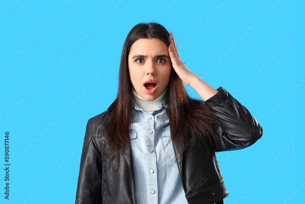 Shocked young woman in leather jacket on blue background