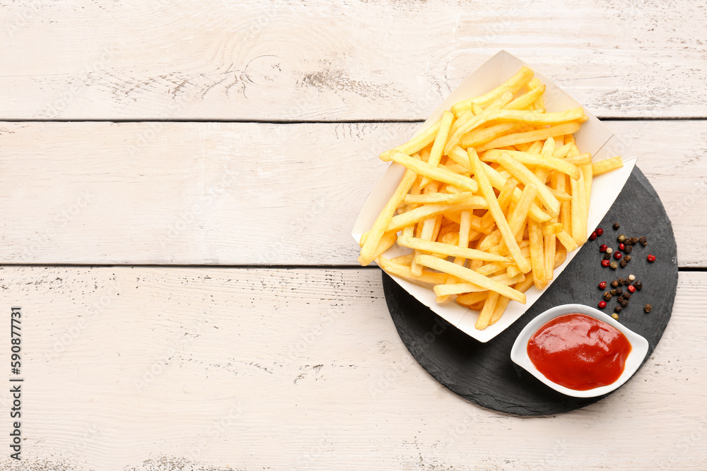 Paper box with tasty french fries, ketchup and pepper on light wooden background