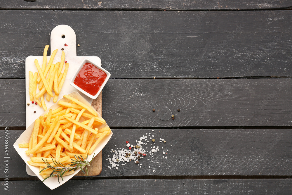 Paper box with tasty french fries, spices and ketchup on dark wooden background