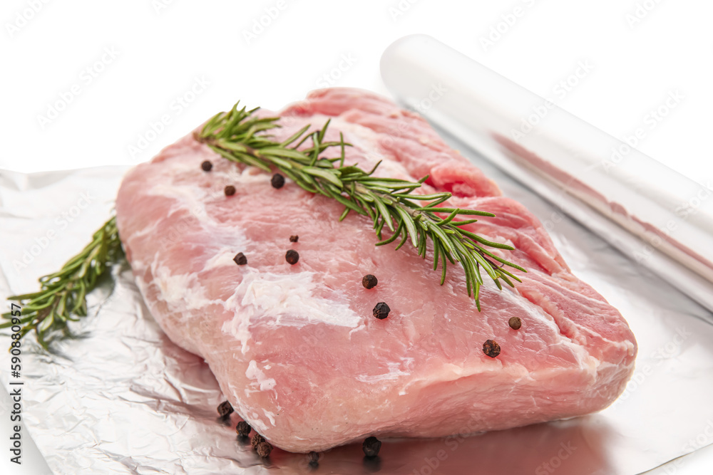 Aluminium foil roll with piece of raw meat, rosemary and peppercorns on white background, closeup