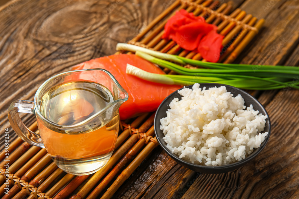 Bamboo mat with vinegar, boiled rice, salmon, ginger and green onion on wooden background