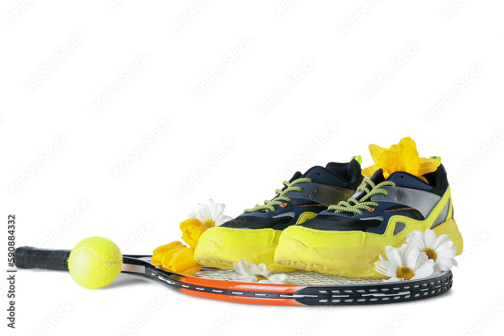 Sneakers with spring flowers, ball and tennis racket on table against white background