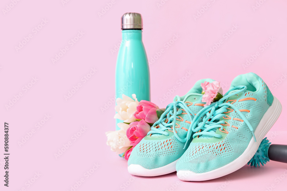 Sneakers with spring flowers, massage roller and bottle on pink background