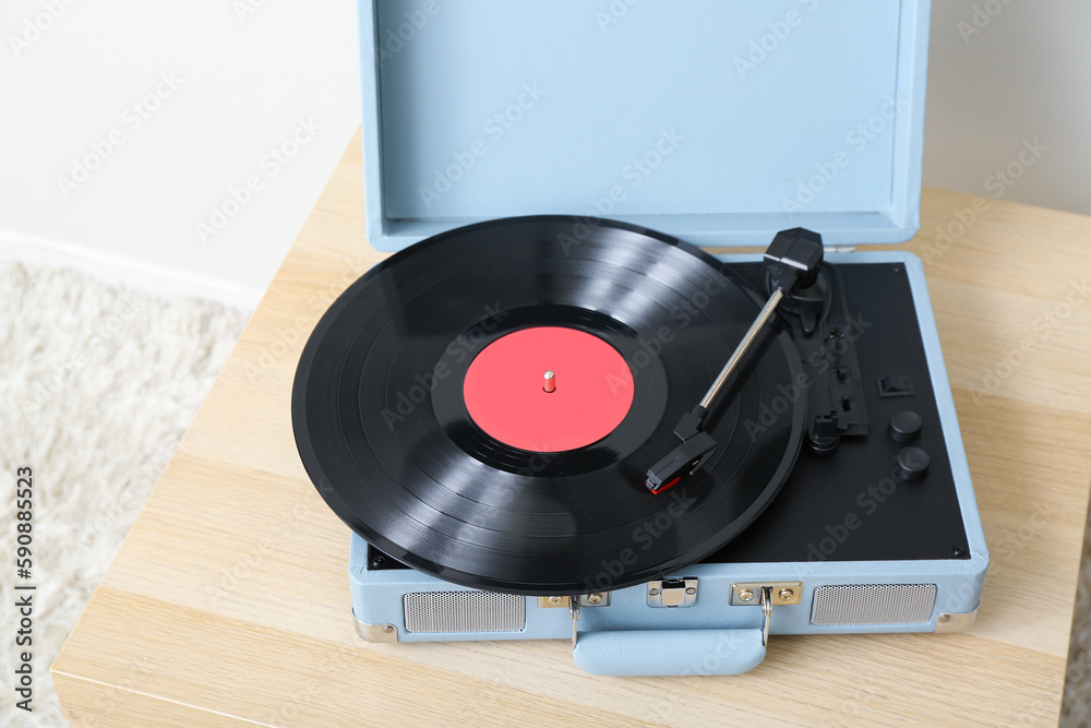 Record player with vinyl disk on table near light wall in room, closeup