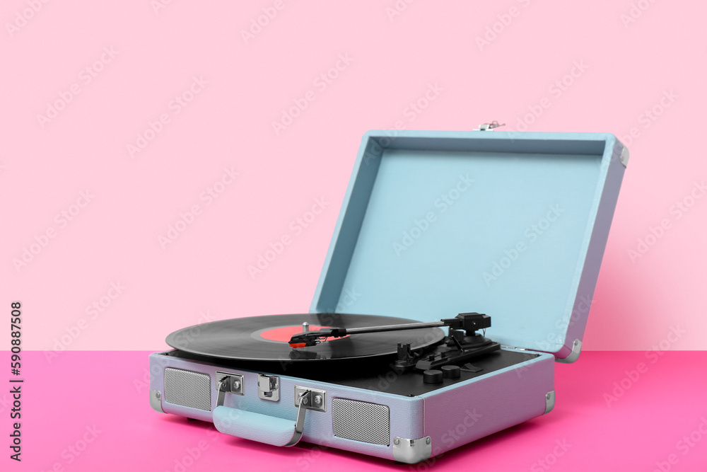 Record player with vinyl disk on table near pink wall