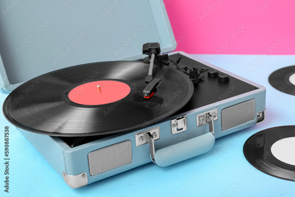 Record player with vinyl disks on table near pink wall