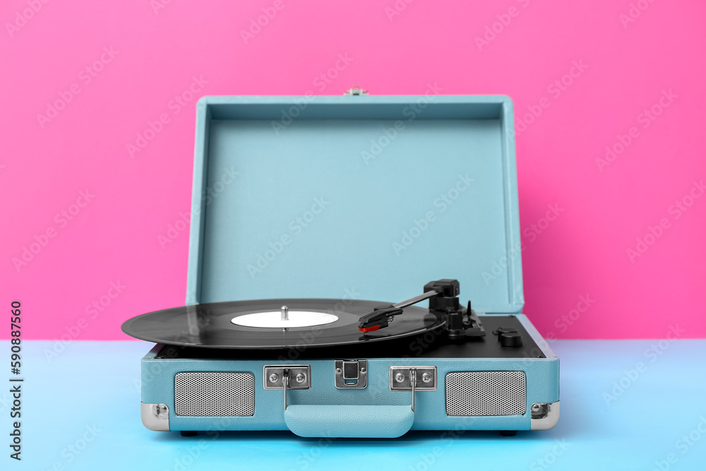 Record player with vinyl disk on table near pink wall