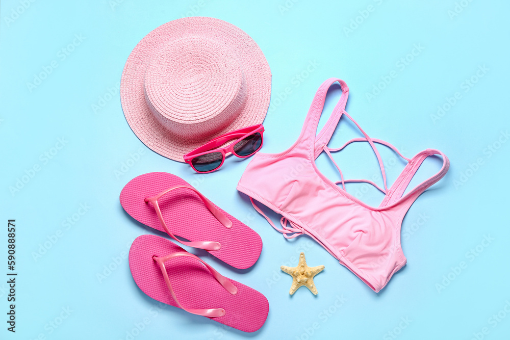 Flip-flops with swimsuit, sunglasses, hat and starfish on blue background