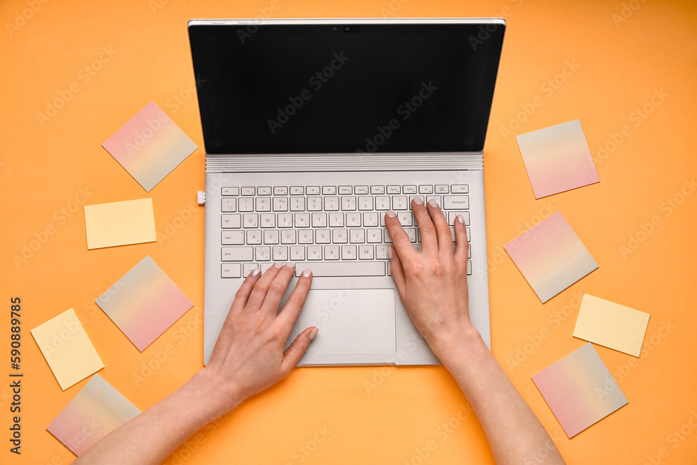 Female hands with modern laptop and sticky notes on orange background