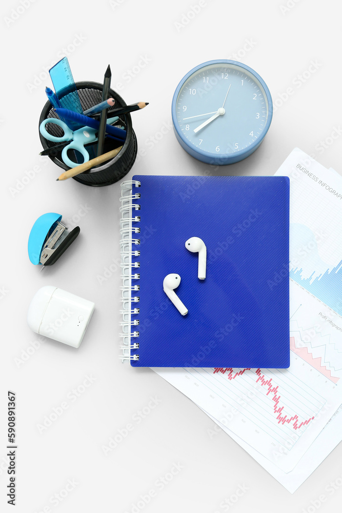 Composition with notepad, clock, stationery and earphones on light background