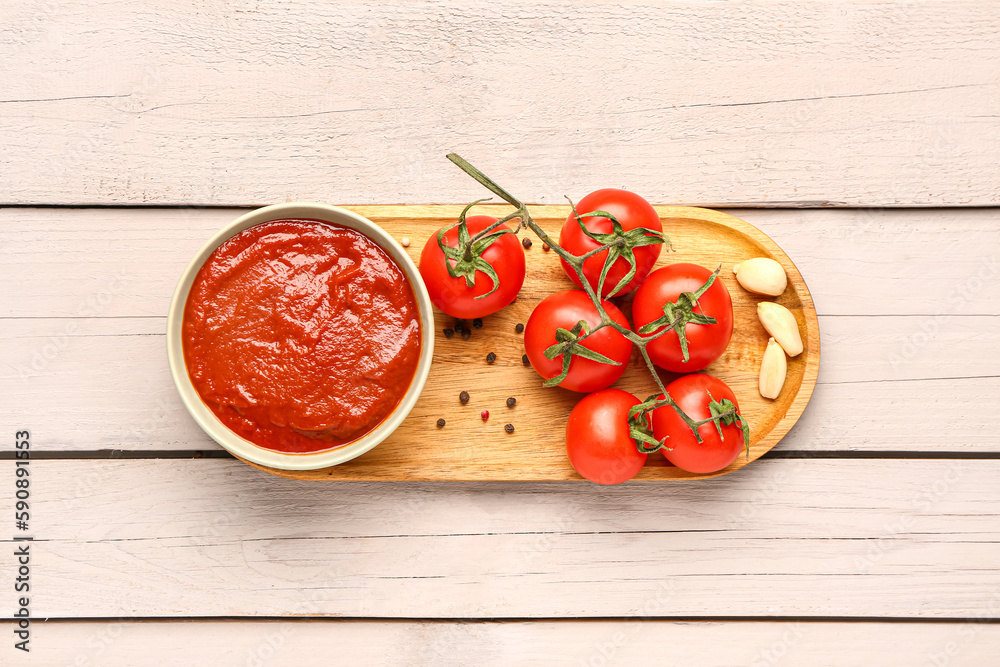 Bowl with tasty tomato paste and fresh vegetables on light wooden background