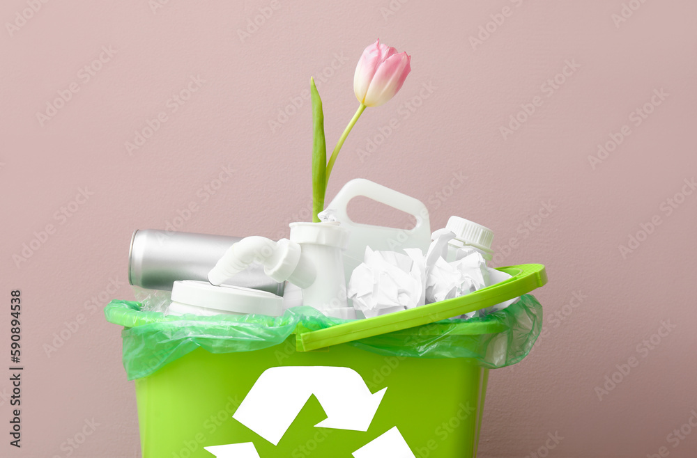 Recycling bin with garbage and tulip near pink wall, closeup