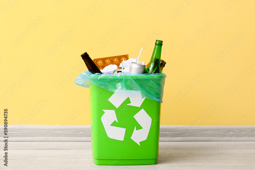 Recycling bin with garbage near yellow wall