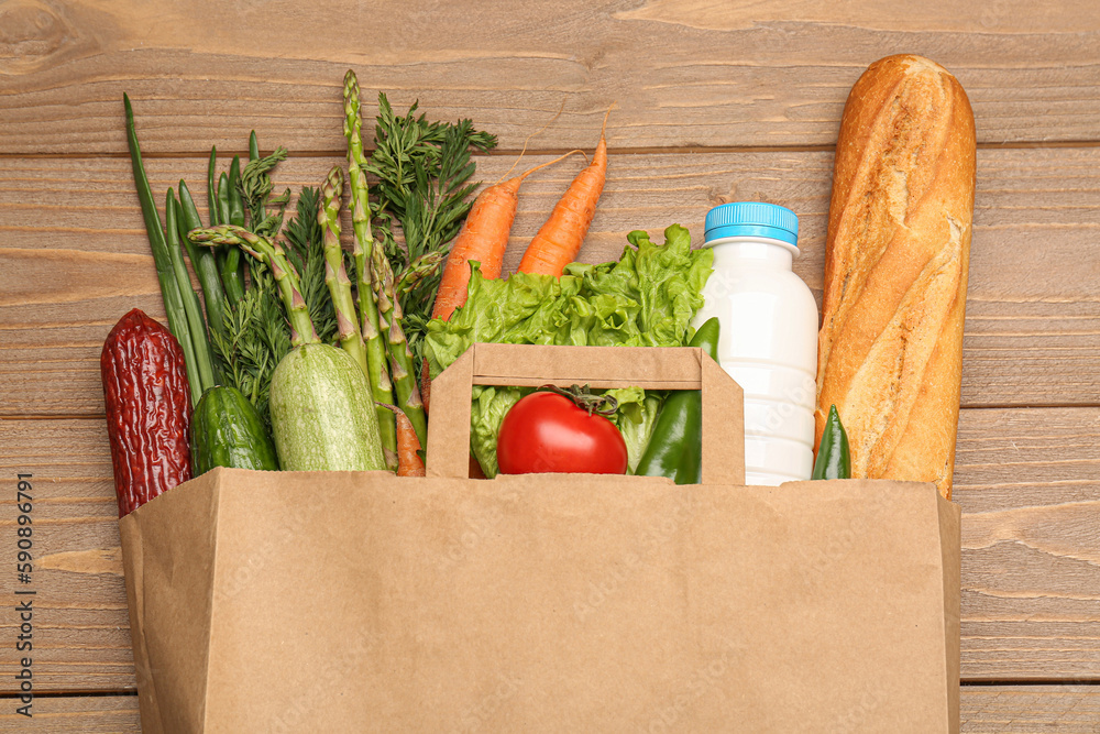 Paper bag with vegetables, milk and bread on wooden background