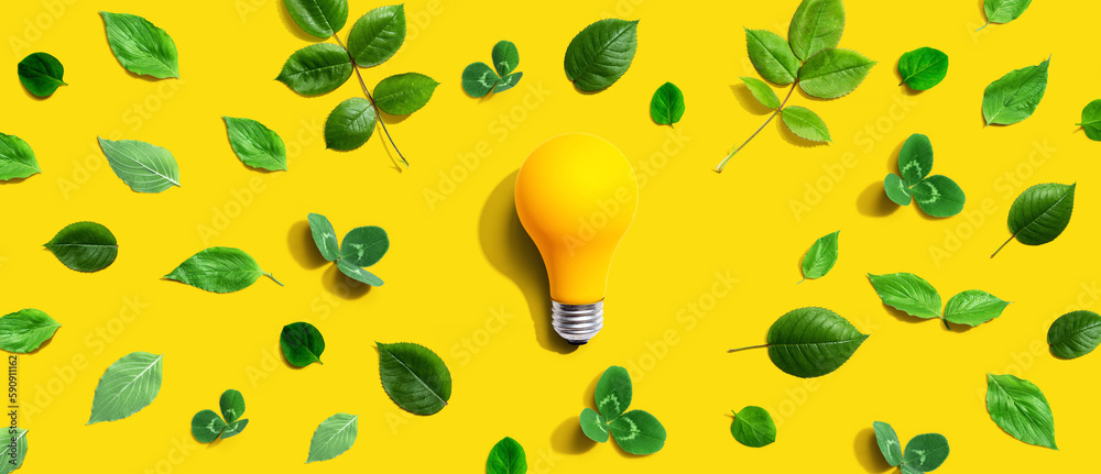 Yellow light bulb with green leaves - Flat lay