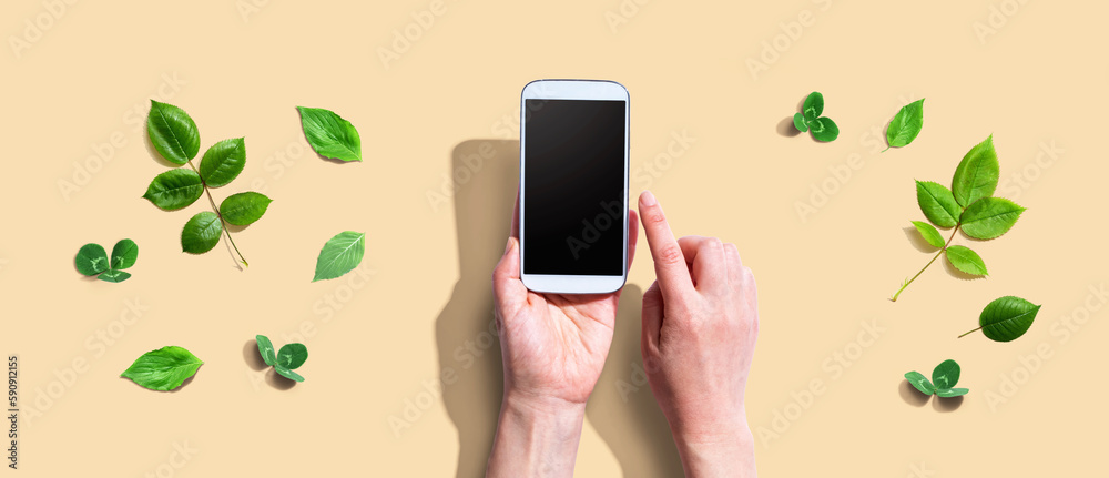 Person using a smartphone with green leaves - flat lay