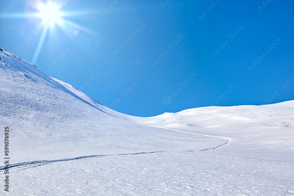 Landscape of East Greenland with mountains, snow, blue sky and sun