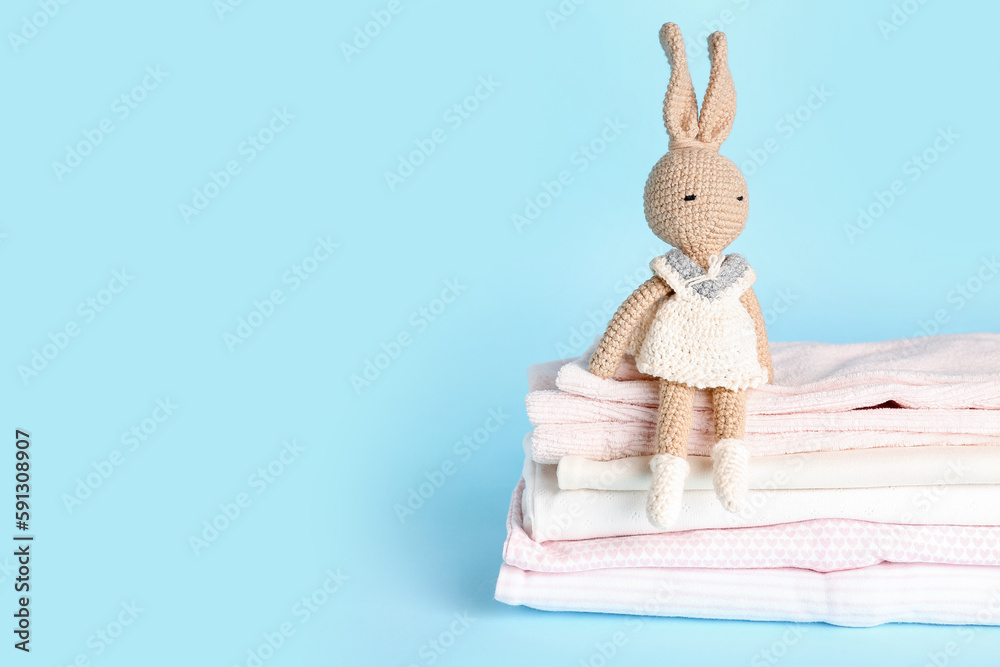 Stack of different baby clothes and toy on color background