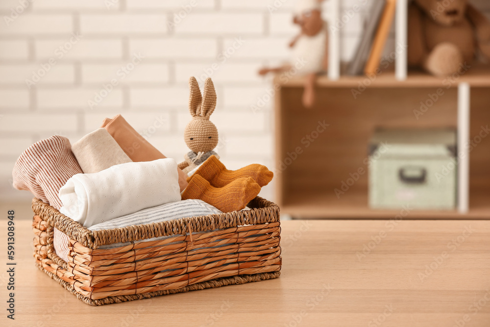 Basket with baby clothes and toy on wooden table