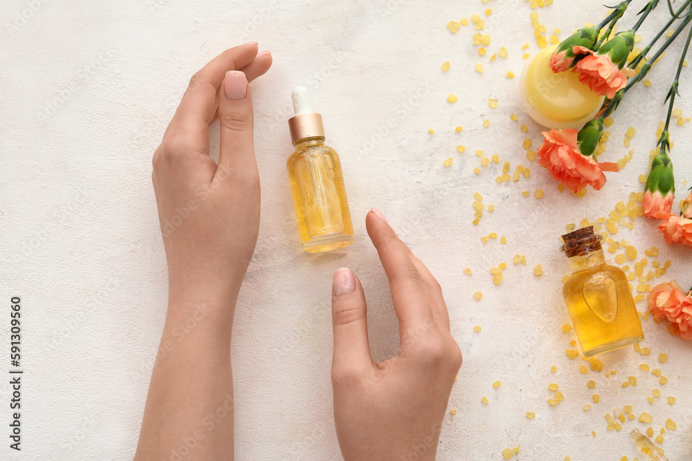 Female hands with cuticle oil, cosmetics and carnation flowers on light background