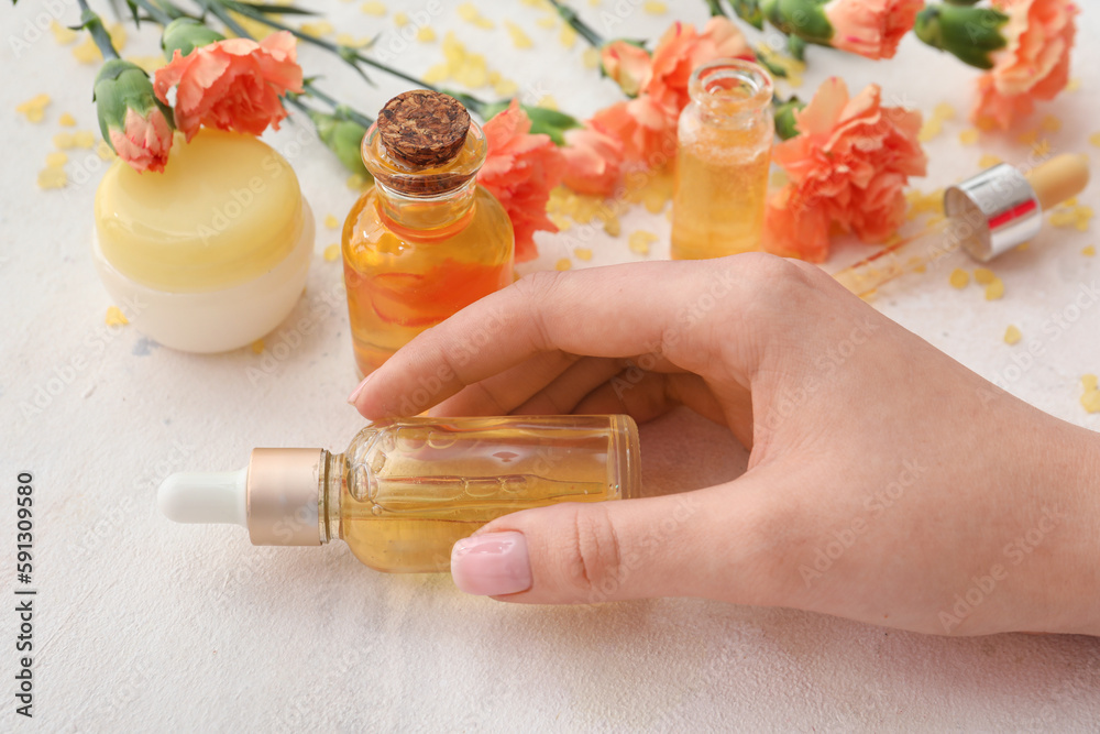 Female hand with cuticle oil, cosmetics and carnation flowers on light background, closeup