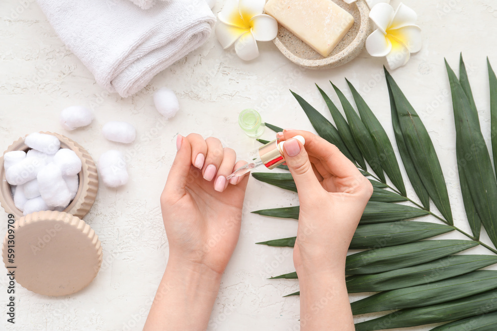 Female hands with bottle of cuticle oil, bath supplies and palm leaf on light background