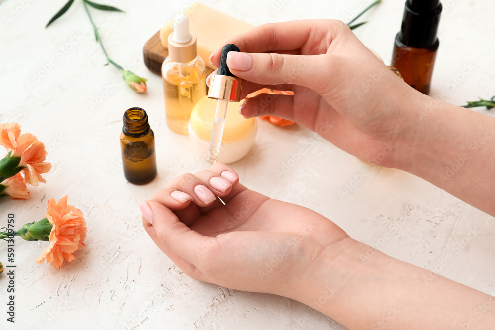 Woman applying healthy oil onto cuticles on light background, closeup