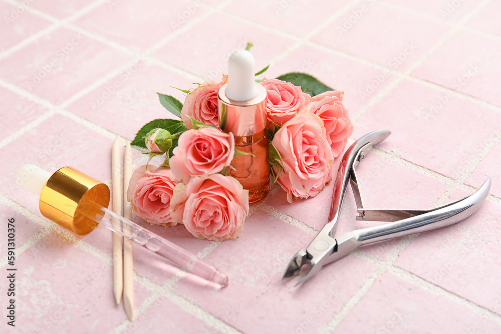 Composition with bottle of cuticle oil, manicure instruments and rose flowers on color tile backgrou