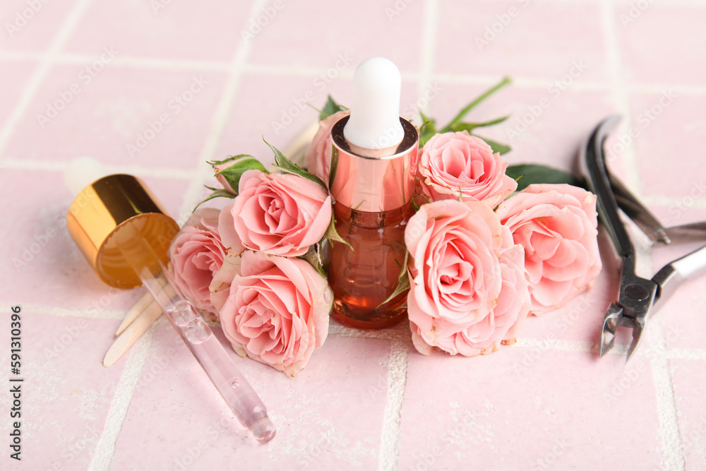 Composition with bottle of cuticle oil, manicure instruments and rose flowers on color tile backgrou