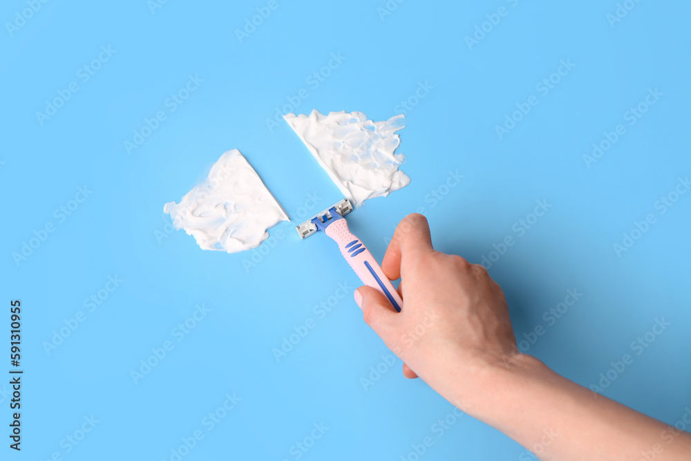 Female hand with safety razor and shaving foam on color background