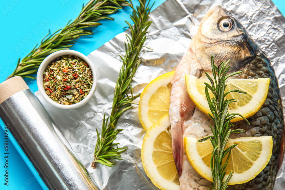 Aluminium foil roll with fresh raw fish, lemon slices, rosemary and spices on color background, clos