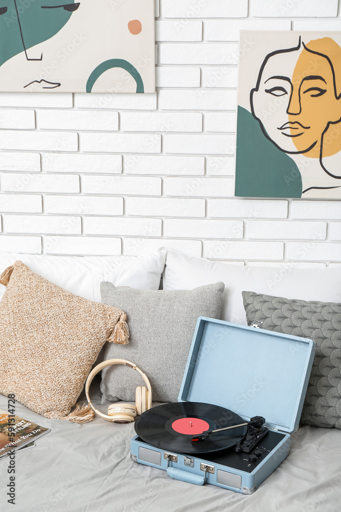 Record player with vinyl disk and headphones on bed in room