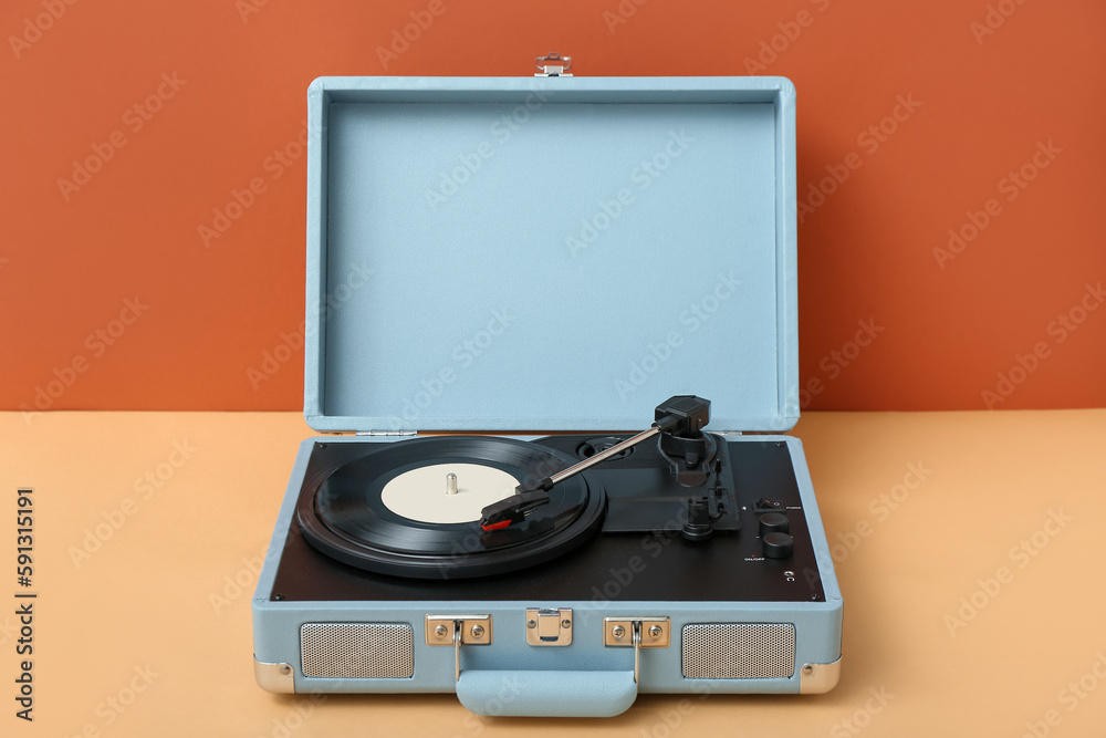 Record player with vinyl disk on table near orange wall