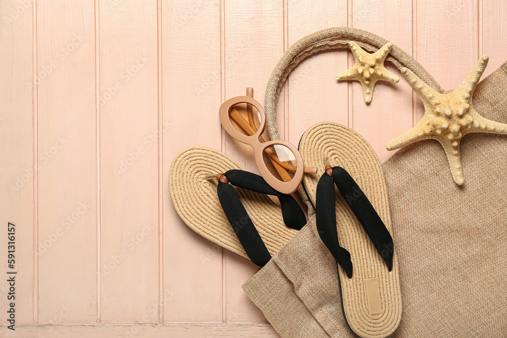 Flip-flops with sunglasses, starfishes and bag on beige wooden background