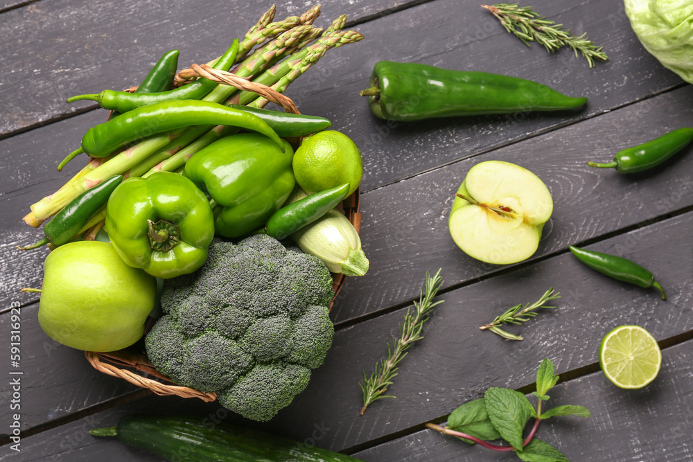 Basket with different fresh vegetables and fruits on black wooden background