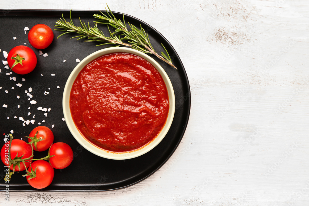 Bowl with tasty tomato paste and fresh vegetables on light wooden background