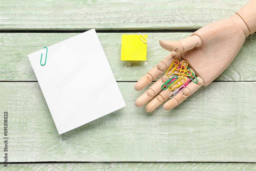 Sticky note and wooden hand with paper clip on green wooden background