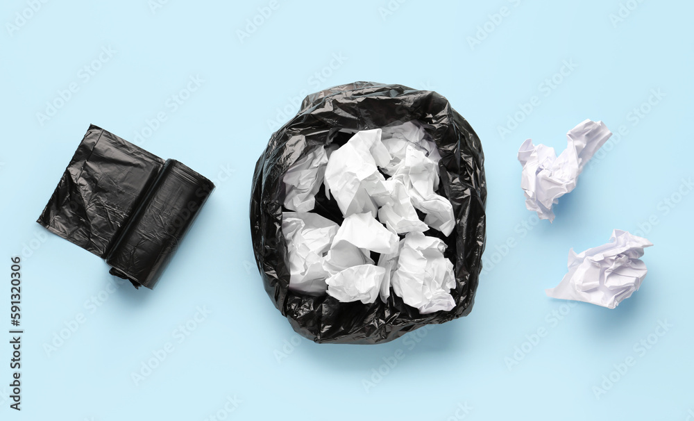 Black roll of garbage bags and rubbish bin with crumpled paper on blue background