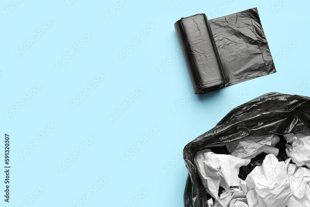 Black roll of garbage bags and rubbish bin with crumpled paper on blue background